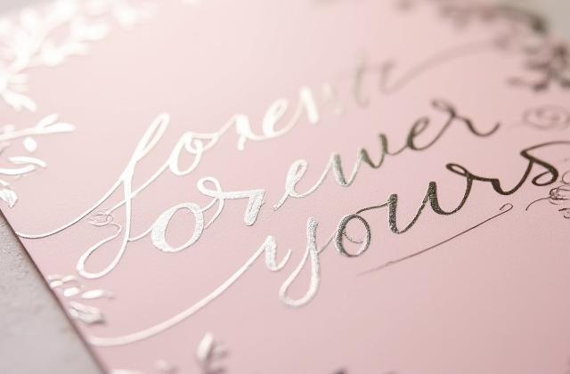 Soft silver foil floral line-art pattern on a blush pink wedding invitation, conveying romance and elegance.